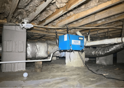 A crawlspace with exposed batt insulation and a dehumidifier installed, showcasing deteriorating insulation and ventilation ducts.