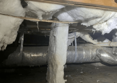 Close-up of deteriorating batt insulation hanging from the ceiling of a crawlspace, with insulation falling onto the ground.